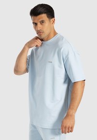 T-shirt oversized in cotone azzurro chiaro con maniche corte, colletto a girocollo e un piccolo logo sul petto. Texture liscia e vestibilità comoda.
