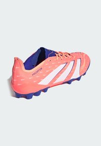 Scarpe da calcio con una tomaia corallo vivace, dettagli blu, tre strisce bianche, superficie testurizzata e tacchetti viola modellati.