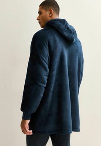 Donkerblauwe fleece oversized hoodie met een zachte textuur, grote capuchon en losse mouwen, gezien vanuit de achterkant.