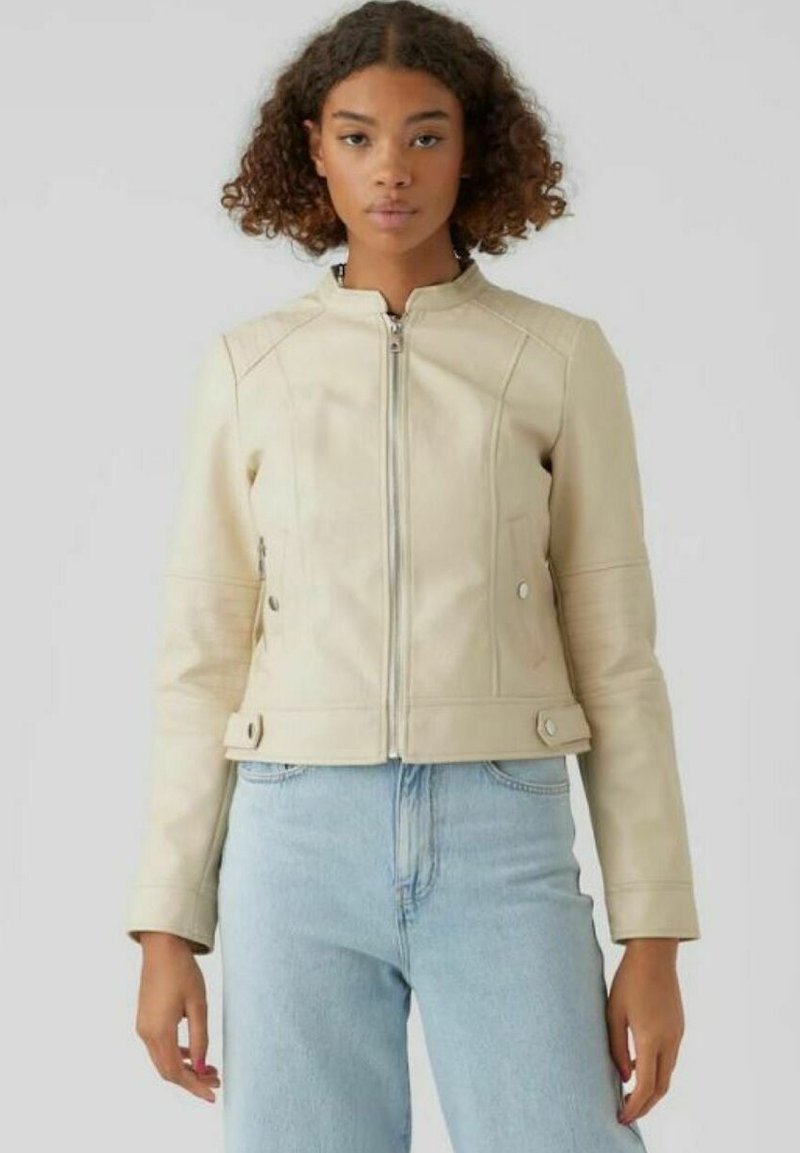 Giacca in pelle beige con una forma aderente, chiusura con zip e tasche laterali. Presenta dettagli delle cuciture sulle spalle e sui polsini.