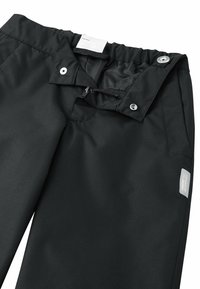 Schwarze wasserdichte Hose mit elastischem Bund, Reißverschluss und Druckknopf. Auffälliges Logotag an der rechten Seite. Glatte Textur.