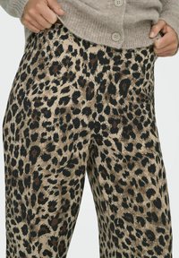 Beige wijdvallende broek met panterprint, voorzien van donkerbruine en zwarte vlekken. Gemaakt van zachte stof, met een vloeiende en ontspannen pasvorm.