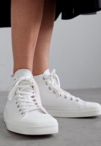 Vita höga sneakers i canvas med texturerad yta, utrustade med metallögon, snören och en gummisula.