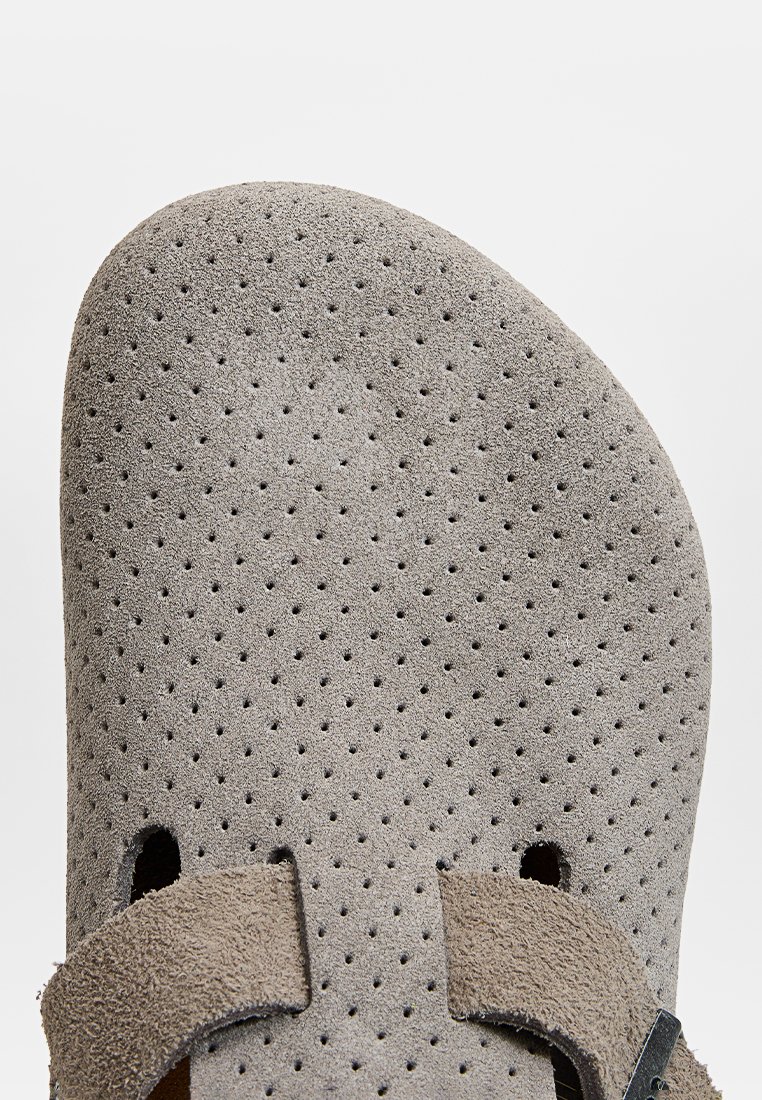 Graue Wildledersandale mit durchbrochener Gestaltung, verstellbaren Riemen und schwarzem Zubehör. Glatte Textur mit abgerundeter Spitze und offenen Seiten für Belüftung.