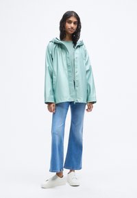 Ανοιχτό τιρκουάζ αδιάβροχο μπουφάν με κουκούλα, πατιλέτα με κουμπιά και εμπρόσθιες τσέπες. Συνδυασμένο με καμπάνα μπλε τζιν και λευκά αθλητικά παπούτσια. Λείο υλικό.