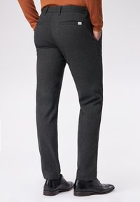 Dunkelgraue, maßgeschneiderte Hose aus strukturiertem Material, mit seitlichen und Gesäßtaschen. Getragen mit schwarzenEleganzschuhen.