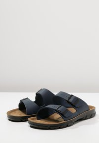 Navy blue slip-on sandals with two adjustable straps, cork footbed, and textured black rubber sole. Features metal buckles for secure fit.