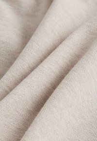 Beige vävt tyg som visar en diagonal struktur med en mjuk känsla. Materialet verkar vara lätt med fina, sammanvävda trådar.