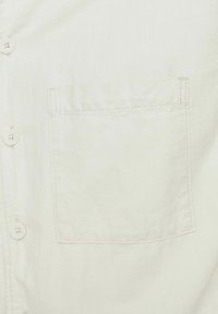 Helles beiges Hemd mit Knopfleiste und einer Brusttasche, aus weichem Stoff gefertigt. Verfügt über einen klassischen Kragen und eine detaillierte Naht an der Tasche.