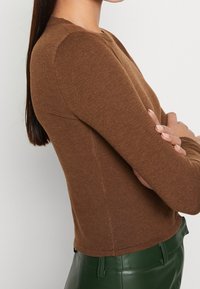 Brązowa, prążkowana bluzka z długim rękawem o okrągłym dekolcie i dopasowanym kroju, zestawiona z zielonymi skórzanymi spodniami. Miękka tkanina i elastyczny krój.
