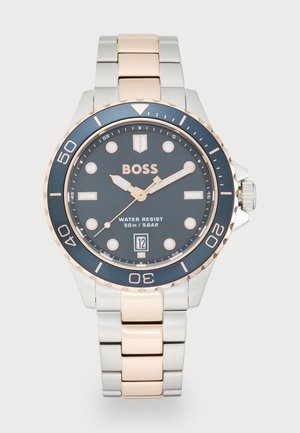 Stainless steel and rose gold watch with a dark gray dial, round face, luminous markers, date display, and diver bezel. Water-resistant to 50m.