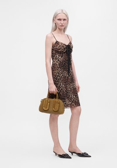 Femme aux cheveux clairs portant une robe sans manches à imprimé léopard, tenant un sac à main marron et portant des mules noires à talons.
