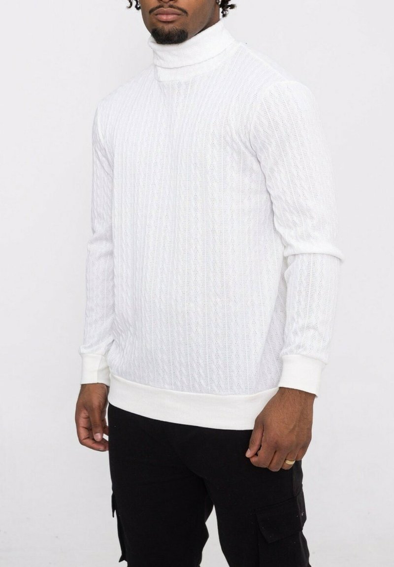 Pull en col roulé blanc avec un motif texturé et côtelé, au design ajusté. Manches longues avec des poignets côtelés, porté avec un pantalon cargo noir.