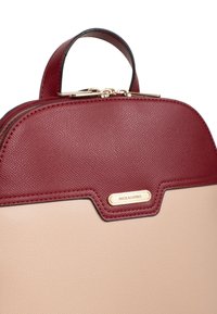 Borsa a mano in pelle strutturata rossa e beige con parte superiore arrotondata, superficie testurizzata, accessori in oro e un logo prominente sulla parte anteriore.