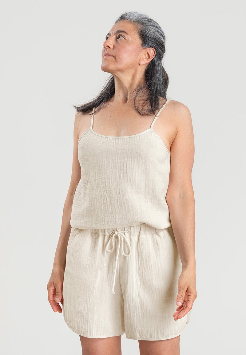 Lichtbeige tweedelig outfit met een mouwloze top met dunne bandjes en elastische shorts met een trekkoord in de taille. Gekreukt textuur.