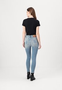 Fekete rövidujjú póló világoskék skinny farmernadrággal párosítva. A farmer nadrág elhasználódott textúrájú, klasszikus zsebekkel rendelkezik, és egy barna bőr folt található rajta. Fekete bokacsizma.