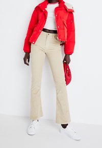 Röd puffjacka med dragkedja och beigerandiga vida kordbyxor. Vita sneakers och en texturerad röd väska fulländar outfiten.