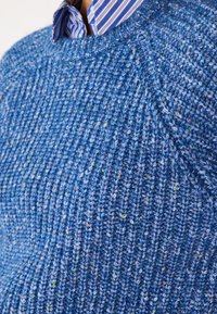 Maglione blu lavorato a maglia con un motivo a coste testurizzato. Presenta macchie multicolori, scollatura rotonda e un colletto a strisce a strati sotto.