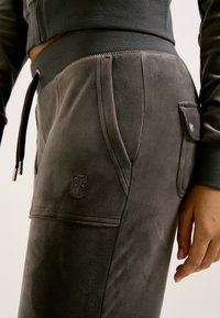 Grijze sweatpants gemaakt van zachte stof met een gladde textuur, voorzien van zijzakken en een gestikt logo-detail aan de voorkant.