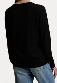 Svart tröja med långa ärmar, subtil textur, rund halsringning och avslappnad passform, kombinerad med ljusblå jeans. Bakifrån visad.