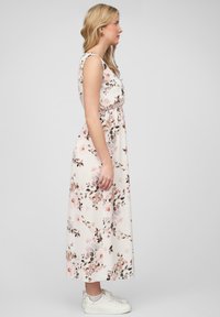 Florale maxi-jurk in lichtcrème met een roze en groene botanische print. Mouwloos ontwerp, ontspannen pasvorm, gecombineerd met witte sneakers.