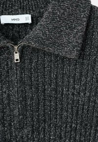 Sweter dzianinowy w ciemnoszarym kolorze z kołnierzem na zamek. Charakteryzuje się pionową fakturą prążkowaną oraz metalicznym suwakiem. Widoczna etykieta.