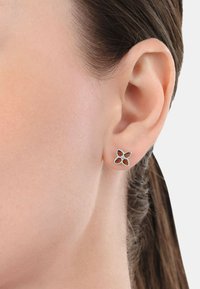 Pendientes de plata en un diseño floral, con cuatro formas de pétalos, cada una con un centro cortado y adornados con pequeños rhinestones blancos.