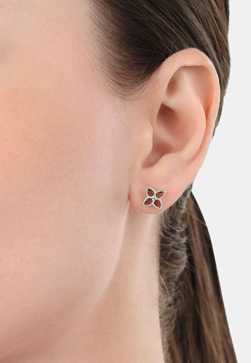 Pendientes de plata en un diseño floral, con cuatro formas de pétalos, cada una con un centro cortado y adornados con pequeños rhinestones blancos.