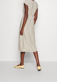 Béžové midi šaty s vertikálními černými pruhy, krátkými rukávy, stahovaným pasem a postranními kapsami. Nosené s žlutými balerínami.