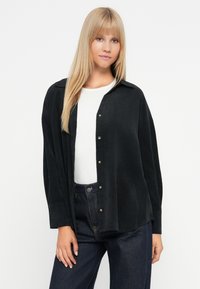 Czarna koszula zapinana na guziki z kołnierzykiem, długimi rękawami i luźnym krojem. Wykonana z gładkiego materiału z metalowymi guzikami i subtelną fakturą.