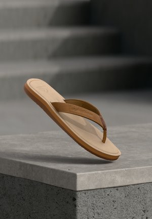 Smeđa i bež japanka nagnuta na svijetlosivoj kameno površini s zamagljenim stepenicama u pozadini.