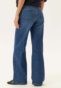 Ufsade denimjeans i mörkblått, med två bakfickor och en slät textur. Midjan är klassisk med bälteshällor.