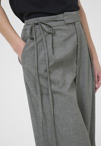 Pantalones de raya gris con cintura alta, cinturón de lazo y bolsillos laterales. Tejido suave con una textura lisa y un corte ajustado.