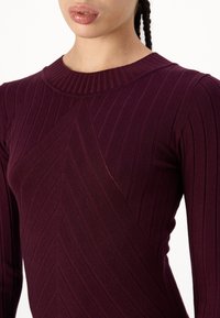 Top in magenta a costine con scollatura rotonda e motivi testurizzati diagonali, che esaltano una silhouette aderente e un tessuto liscio.