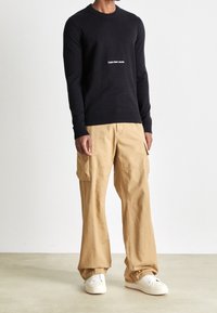 Marinblå tröja med rund hals och vitt logo; kombinerad med khakifärgade cargobyxor med sidofickor; vita sneakers fulländar outfiten.