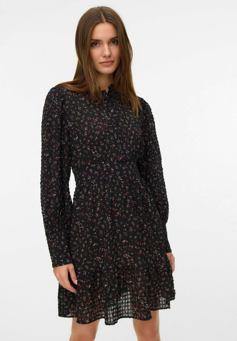 Robe noire à manches longues, ornée d'un motif floral rouge et blanc, avec un devant boutonné et un ourlet évasé au fini texturé.
