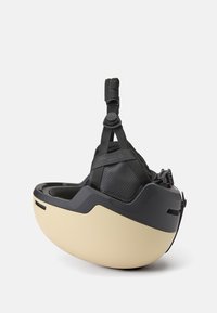 Czarny i beżowy ergonomiczny kask o opływowym kształcie, z regulowanymi paskami i perforowaną czarną wyściółką dla lepszej wentylacji.