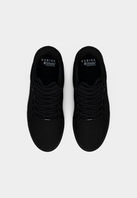 Ζευγάρι μαύρα αθλητικά παπούτσια Nubikk με ενθέματα άνεσης Ortholite, επίπεδα μαύρα κορδόνια και λείο υφή, εμφανίζονται από πάνω σε λευκό φόντο.