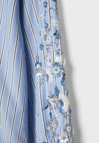 Modrý a biely pásikavý textil s detailným 3D kvetinovým výšivkov a striebornými flitrami zoskupenými pozdĺž jedného okraja.