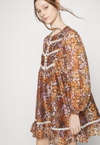 Vestido fluido feito de tecido leve, apresentando um padrão floral castanho com realces em laranja, roxo e branco, com acabamento em renda e mangas bufantes.