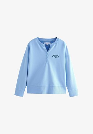 Gaiši zila pēdēna ar brīvu piegriezumu, apaļu kakla izgriezumu un trīs pogu slēdzēju. Iekļauj priekšējo krūšu izšuvumu un ribota piedurknes.