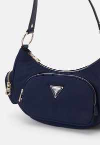 Sac à épaule Guess bleu marine avec fermetures éclair dorées, poche avant, logo triangulaire et sangle réglable avec détail anneau doré.
