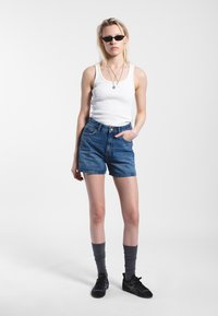 Denim shorts with high waist and back pockets, paired with a white ribbed tank top and black sneakers, complemented by grey knee socks.