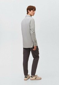 Polo a maniche lunghe grigio chiaro, vestibilità rilassata, vista posteriore, abbinato a pantaloni cargo scuri e sneaker beige. Design minimal, senza motivi visibili.