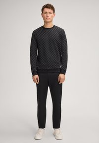 Czarny sweter z wzorem o fakturowanym designie, okrągłym dekoltem i prążkowanymi mankietami, w połączeniu z wąskimi czarnymi spodniami i białymi trampkami.