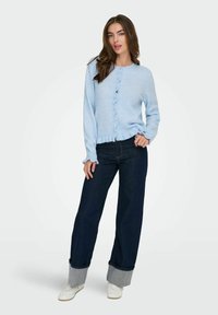 Ljusblå cardigan med rundad, scallopformad knappslå och ribbad nederkant, som matchas med mörk denimvidbyxor med uppvikta nederkanter.