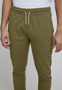 Olivgrüne Jogginghose mit Kordelzugbund. Hergestellt aus weichem Stoff, mit feinen Nähten und einem kleinen gestickten Logo an der Seite.
