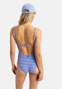 Maillot de bain rayé bleu et blanc avec un design à dos nu et de fines bretelles, associé à une casquette bleu clair. Texture lisse, forme ajustée.