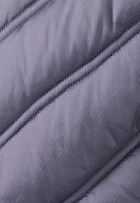 Tessuto grigio trapuntato con una texture liscia. Presenta cuciture diagonali e una leggera lucentezza, che indicano isolamento e durata.