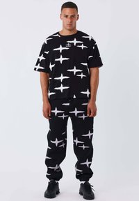 Ensemble noir assorti composé d'une chemise à manches courtes et d'un pantalon, orné d'un motif d'éclat d'étoile blanc. Fabriqué en tissu doux et texturé.